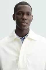 Cazadora tipo canguro de calce relajado, color blanco roto o crema, confeccionada en mezcla de lyocell y algodón. Presenta cuello solapa con cierre frontal de botonadura oculta, manga larga con puños elásticos y bolsillos frontales de vivo. El bajo es ajustable con elástico oculto en los laterales.