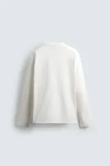 Camiseta de manga larga con corte relajado, confeccionada en tejido compacto de algodón. Presenta cuello redondo acabado en rib y detalle de costura central en la espalda.