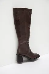 Bota bucanera de caña alta confeccionada en cuero con textura de efecto croco. Presenta un diseño de punta redondeada, cierre lateral y taco cuadrado de altura media.