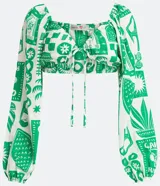 Blusa cropped blanca con estampado de motivos verdes, escote corazón con lazo, mangas largas abullonadas y confeccionada en tricolina.