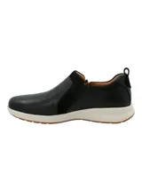 Zapatilla tipo slip-on Hush Puppies modelo Spinal, confeccionada en cuero negro con detalles en gamuza y cierre lateral. Cuenta con una suela de goma blanca con base antideslizante y tecnología de amortiguación.