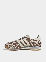 Championes Adidas modelo SL 72 OG con diseño de perfil bajo. Presentan una parte superior de piel con acabado de pelo de poni con estampado animal print de manchas marrones y blancas. Incluyen las icónicas tres tiras laterales en color crema, cordones celestes y suela de goma con entresuela de EVA.