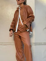 Camisa de cuero sintético color marrón, con cuello redondo, cierre frontal de botones y mangas largas con diseño fruncido y volados en los puños.