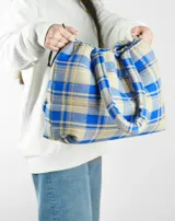 Bolso tipo tote bag de franela a cuadros en tonos azul y beige, con asas tubulares acolchadas y cierre con cordón ajustable.
