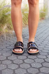 Sandalias bajas de cuero color marrón con tiras de cuero charol negro y hebilla metálica.