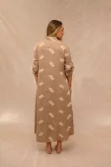Vestido largo estilo camisero de color beige con estampado de plumas en tono más claro, cuello camisero, botonadura frontal completa, bolsillos laterales y mangas largas con presilla para arremangarlas.