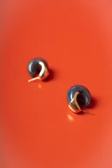 Aros tipo argolla pequeña con diseño semicircular, combinando una pieza de resina jaspeada en tonos azul oscuro con un detalle metálico dorado brillante.