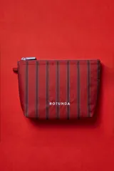Necessaire de diseño rectangular con cierre superior, confeccionada en tela técnica con estampado de rayas verticales en tonos rojizos y bordado de la marca Rotunda en el frente.