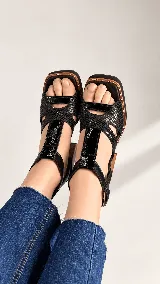 Sandalias negras de tacón ancho con plataforma, confeccionadas en una combinación de texturas que incluye cuero grabado tipo animal print, napa y charol. Cuentan con tiras entrelazadas en la capellada, punta cuadrada y tira ajustable con hebilla lateral en el tobillo. El tacón de 8,5 cm presenta un acabado símil madera.