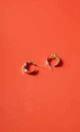 Par de aros tipo argolla pequeños, de color dorado con diseño irregular y acabado brillante.