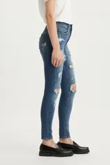 Jean de corte skinny y tiro alto, con diseño de cinco bolsillos y cierre frontal con botón y cremallera. Presenta un acabado lavado con roturas y desgastes localizados en las piernas.