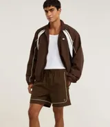 Bermuda deportiva color marrón con piping en color crema, confeccionada en poliamida de secado rápido. Cuenta con cintura elástica con cordón ajustable y bolsillos laterales.