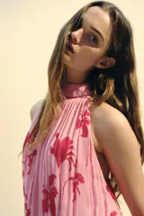 Top sin mangas color rosa con estampado de flores rojas, cuello halter y espalda descubierta.