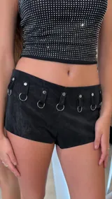 Short negro de tiro bajo confeccionado en eco cuero, con presillas decorativas y argollas metálicas en la cintura.