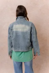 Campera de denim con lavado claro y efecto desgastado. Presenta cuello camisero, cierre frontal con botones metálicos, dos bolsillos frontales con tapa y botón, y puños abotonados.
