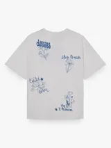 Camiseta de corte oversize, color blanco, con cuello redondo, mangas cortas y estampa botánica pequeña en el pecho.
