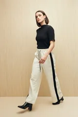 Pantalón de corte recto y holgado, color blanco con franjas laterales negras a contratono. Presenta cintura elástica con cordones ajustables y bolsillos laterales.