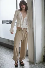 Camisa de gasa color blanco con escote en pico, cierre frontal con lazadas y detalles de volantes. Presenta mangas largas con puños elásticos y terminación en volante, además de bordados a tono.