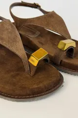 Sandalias de gamuza color tostado, con tira de dedo, hebilla ajustable en el talón y detalle metálico dorado.
