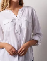 Blusa blanca de lino y rayón, con cuello a la base, escote en V y abertura con botones. Tiene bolsillos en la parte delantera y mangas largas regulables con presilla y botón.