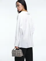 Camisa de corte recto y líneas clásicas, color blanco, con cuello camisero, cierre frontal de botones y puños anchos con botón.