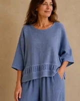 Blusa de lino color azul jean, con cuello redondo, mangas amplias tres cuartos y detalle de volado fruncido en el ruedo.