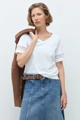 Remera blanca de algodón con cuello en V y mangas cortas que presentan un detalle de puntilla en los bordes.