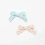 Pack de dos pinzas para el pelo con forma de moño, una celeste lisa y otra color crema con estampado de flores rosas.