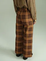 Pantalón de tiro alto con corte ancho y recto, confeccionado en tela de algodón con estampado de cuadros escoceses en tonos azul marino, verde y rojo. Presenta cierre frontal oculto con botones internos y pasacintos en la cintura.