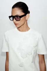 Camiseta blanca de algodón con cuello redondo y manga corta, destacada por aplicación de flores tridimensionales a tono en el frente.