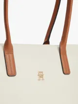 Cartera tote Tommy Hilfiger de nailon color beige, con dos asas superiores de cuero sintético tostado y cierre de cremallera. Presenta el monograma metálico TH en la parte delantera.