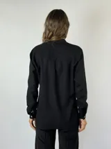 Camisa color mostaza con volados desflecados a lo largo de la botonadura frontal, cuello mao y mangas largas con puños abotonados.