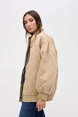 Campera bomber de gabardina con diseño capitoneado, cuello alto, cierre frontal con botones a presión ocultos y mangas abullonadas con puños elásticos.