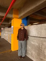 Camisa de lino color marrón con cuello redondo decorado con volados, cierre frontal de botones y mangas largas con puños ajustados.