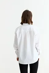 Camisa de manga larga color blanco, con cuello mao y puños con detalle de volados. Presenta cierre frontal con botones y un corte clásico.