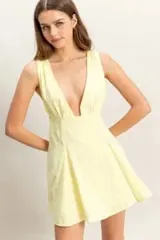 Vestido corto color amarillo pastel, con escote en V profundo, sin mangas y falda acampanada con diseño fresco y ligero.