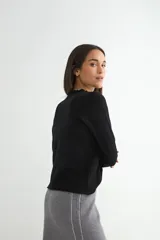 Sweater de punto negro con cuello redondo y detalle de borde ondulado, de manga larga y corte clásico.