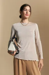 Top de manga larga con cuello redondo, confeccionado en un tejido suave con un sutil acabado satinado. Presenta una silueta ajustada, tajos laterales en el ruedo y terminaciones onduladas.