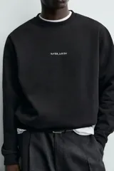 Sudadera de cuello redondo y manga larga, confeccionada en algodón con interior afelpado. Presenta un diseño de corte regular con estampado de texto en contraste en la parte frontal y acabados en rib en puños y ruedo.