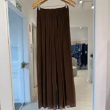 Pantalón marrón de corte ancho y fluido, confeccionado en tejido plisado translúcido con cintura elástica.