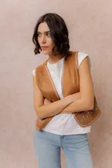 Chaleco corto de efecto gamuza color tostado, con detalles bordados en contraste en los bordes y en la parte inferior. Presenta escote en V y diseño abierto al frente.