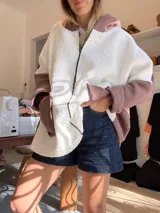 Campera tipo hoodie confeccionada en tejido de corderito sintético con diseño de bloques geométricos en tonos marrón, rosado y blanco. Presenta capucha amplia, corte oversize y mangas largas.