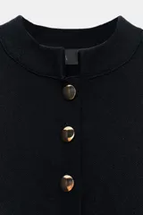 Chaqueta de punto color negro con cuello redondo, manga larga y cierre frontal con botones dorados. Presenta un corte entallado con bajo en evasé.