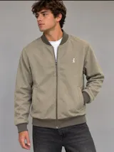 Campera bomber de paño fino en color beige con diseño de espiga sutil, cierre frontal completo, bolsillos laterales ribeteados y puños, cuello y dobladillo en rib elástico marrón oscuro. Cuenta con un pequeño bordado blanco en el pecho.