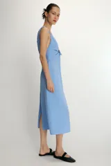 Vestido midi de corte recto con estampado de rayas verticales en tonos azul y blanco. Presenta escote en pico con detalle de abertura ajustable mediante lazada frontal, tirantes anchos con acabado fruncido y cierre lateral con cremallera oculta.