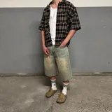 Camisa de manga corta con corte boxy fit, diseño a cuadros en tonos marrones, amarillos y azules, con cierre frontal de botones y bolsillo en el pecho.
