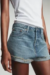 Shorts de jean de algodón, tiro alto, color azul claro desgastado. Presenta cinco bolsillos, cierre frontal con botón metálico y cremallera, y bajo desflecado con vuelta.