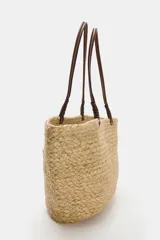 Bolso tipo shopper confeccionado en yute trenzado, con doble asa de mano en cuero sintético color marrón.
