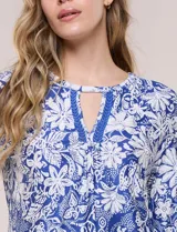 Blusa azul y blanca con estampado floral y geométrico, de calce suelto, con escote redondo, abertura tipo keyhole en el pecho, mangas tres cuartos y ruedo amplio con silueta evasé.