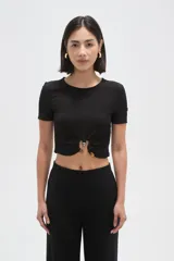 Top de manga corta con textura arrugada, cuello redondo y detalle de frunce frontal con argolla metálica y botón decorativo.